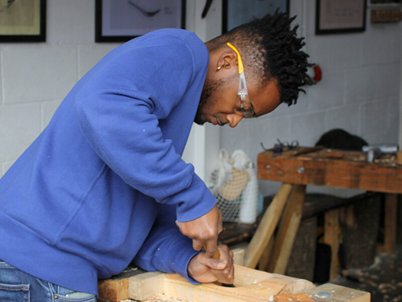 A man is using a chisel to carve wood at a woodworking class